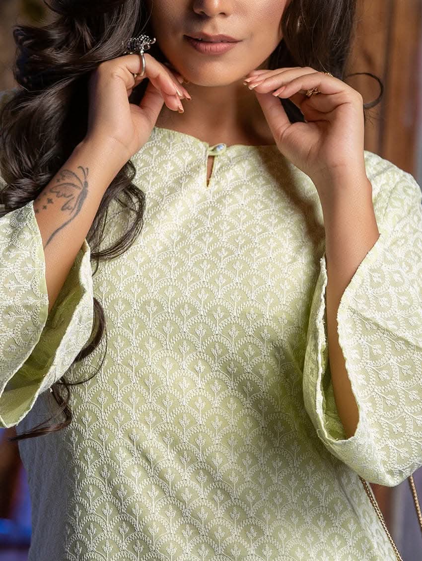 A woman wearing a Green embroidered cotton kurta with a round neckline and three-fourth bell sleeves, standing against a backdrop of a chair and wall.