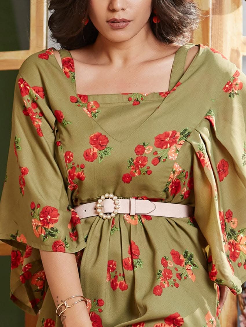 A woman wearing a green floral print tunic with a V-neckline and kaftan-like sleeves. The tunic is double layered, and she is also wearing a belt and sandals.