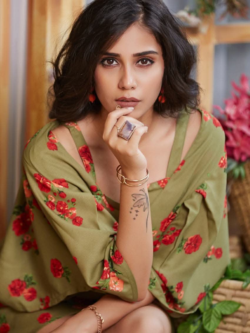 A woman wearing a green floral print tunic with a V-neckline and kaftan-like sleeves. The tunic is double layered, and she is also wearing a belt and sandals.