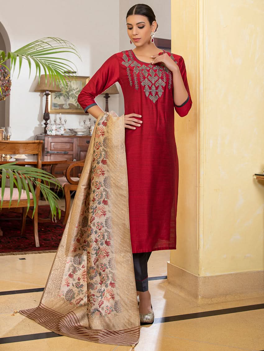 A woman modeling a red raw silk suit set with hand embroidery, consisting of a kurta, pants, and a dupatta with a floral design.