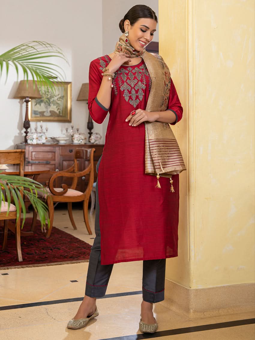 A woman modeling a red raw silk suit set with hand embroidery, consisting of a kurta, pants, and a dupatta with a floral design.
