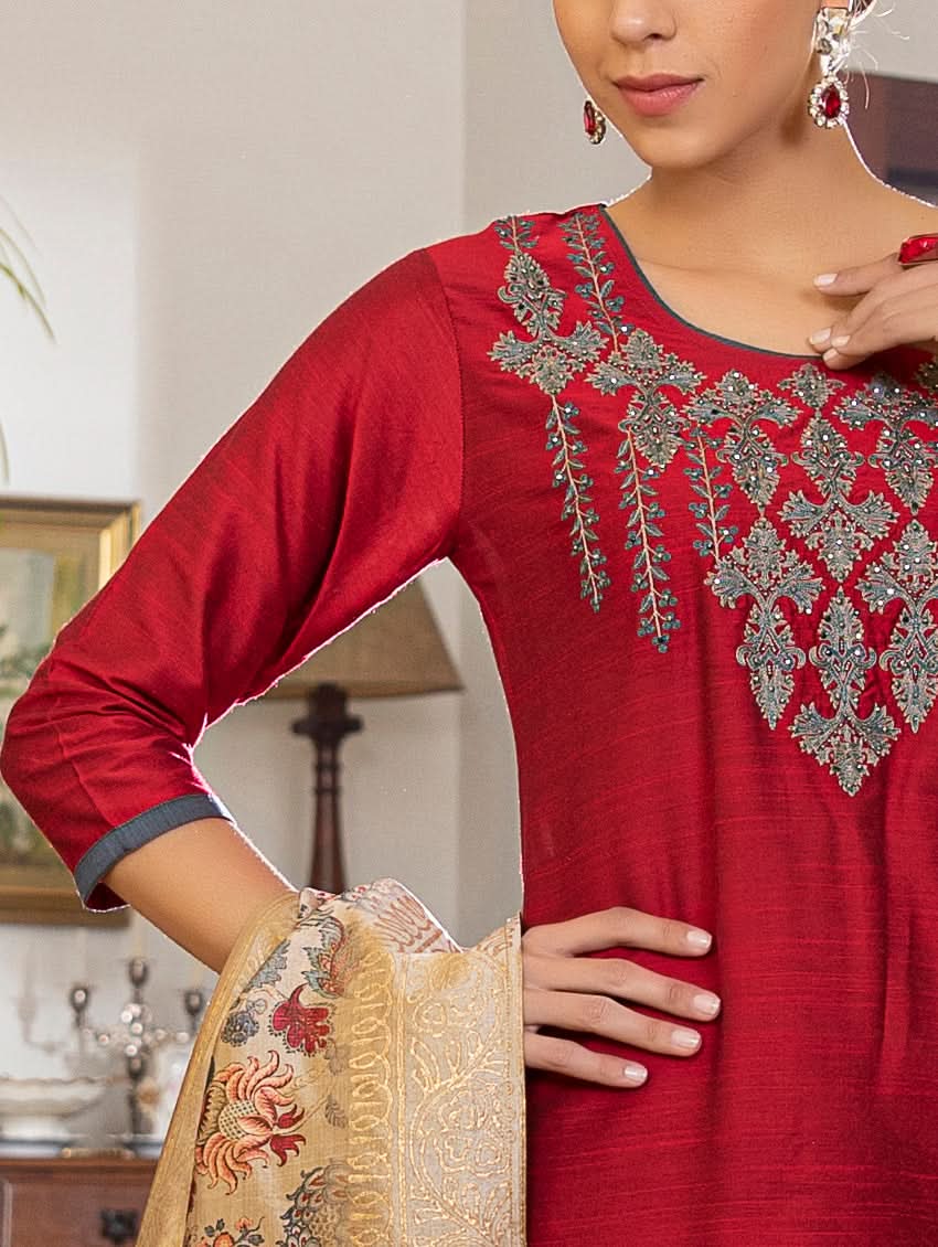 A woman modeling a red raw silk suit set with hand embroidery, consisting of a kurta, pants, and a dupatta with a floral design.