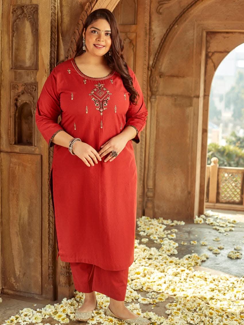 A woman standing in a beautifully decorated room wearing a red handloom cotton kurta with round neckline and three fourth sleeves, featuring computerised thread embroidery.