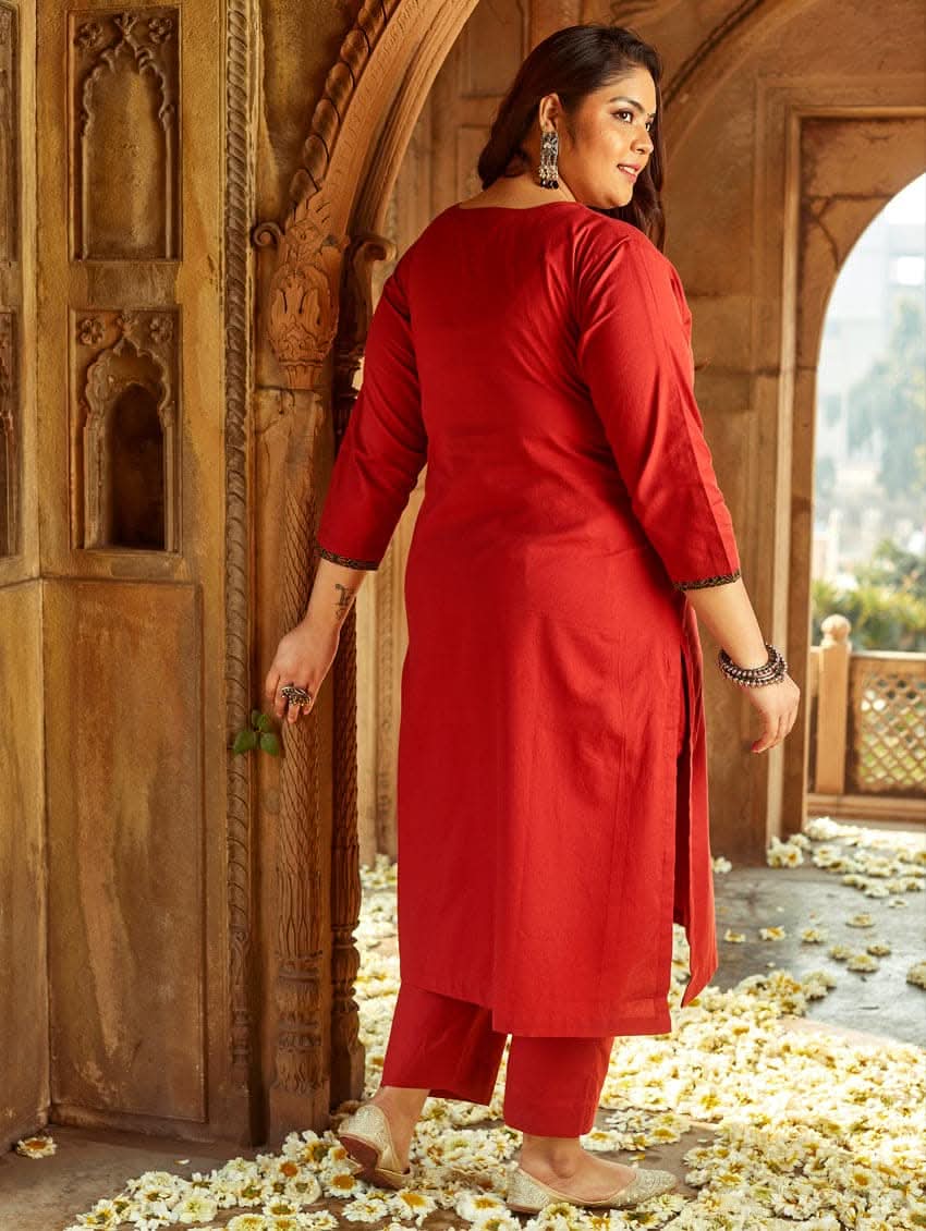 A woman standing in a beautifully decorated room wearing a red handloom cotton kurta with round neckline and three fourth sleeves, featuring computerised thread embroidery.
