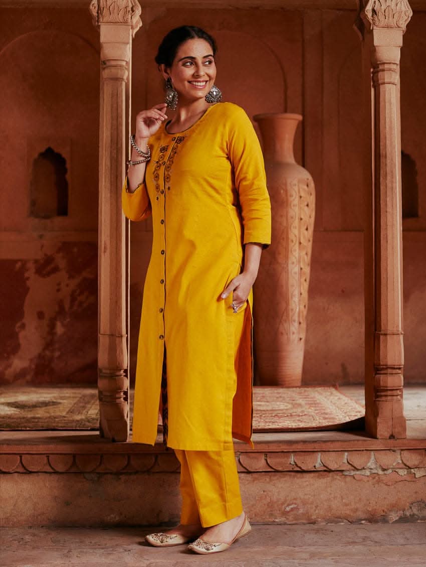 A woman standing in a beautifully decorated room wearing a red handloom cotton kurta with round neckline and three fourth sleeves, featuring computerised thread embroidery.