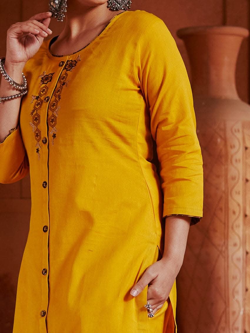 A woman standing in a beautifully decorated room wearing a red handloom cotton kurta with round neckline and three fourth sleeves, featuring computerised thread embroidery.