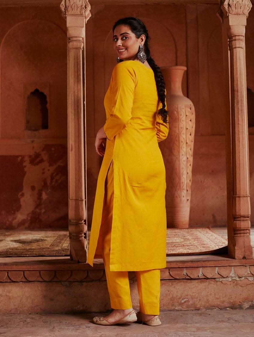 A woman standing in a beautifully decorated room wearing a red handloom cotton kurta with round neckline and three fourth sleeves, featuring computerised thread embroidery.
