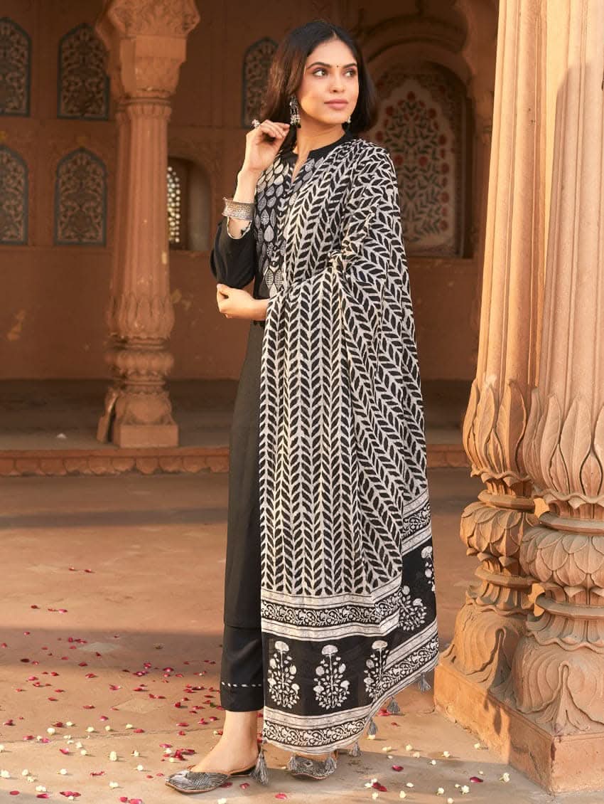 A woman wearing a black rayon suit set with embroidery on the kurta, consisting of a solid colored kurta with pants and a printed mul dupatta.