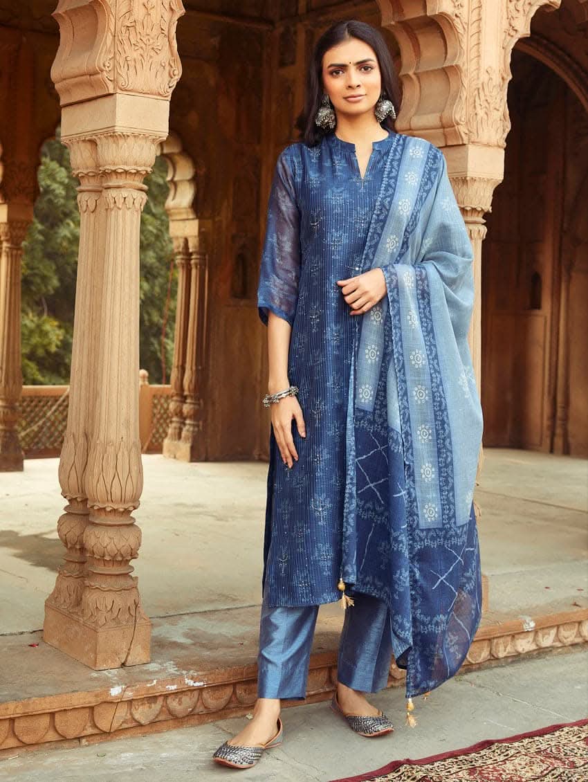 A woman wearing a traditional Digitally Printed Blue Silk Suit Set with a kurta, pants, and dupatta in a historic building with intricate architectural details.