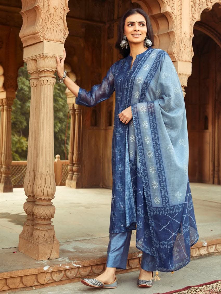 A woman wearing a traditional Digitally Printed Blue Silk Suit Set with a kurta, pants, and dupatta in a historic building with intricate architectural details.
