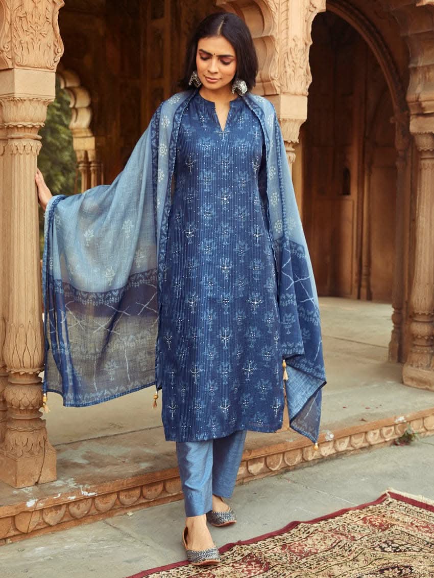A woman wearing a traditional Digitally Printed Blue Silk Suit Set with a kurta, pants, and dupatta in a historic building with intricate architectural details.
