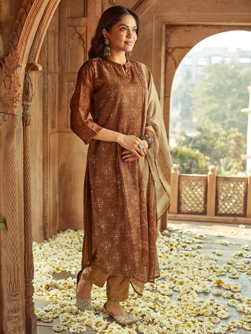 A woman wearing a traditional Digitally Printed Silk Suit Set with a kurta, pants, and dupatta in a historic building with intricate architectural details.