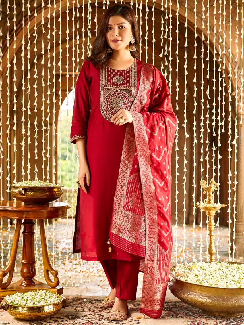 A woman wearing a red silk suit set with embroidered details and a dupatta.