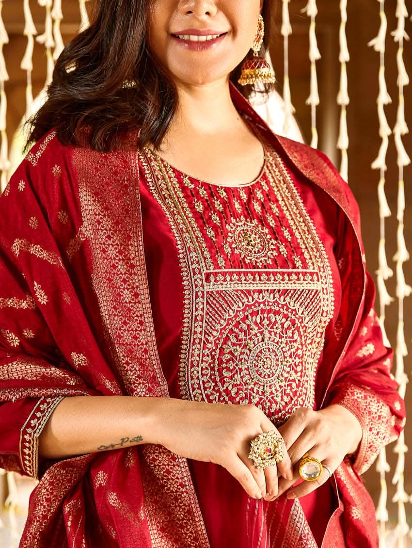 A woman wearing a red silk suit set with embroidered details and a dupatta.