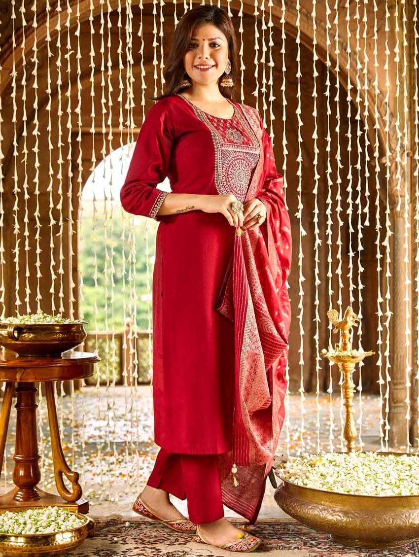 A woman wearing a red silk suit set with embroidered details and a dupatta.
