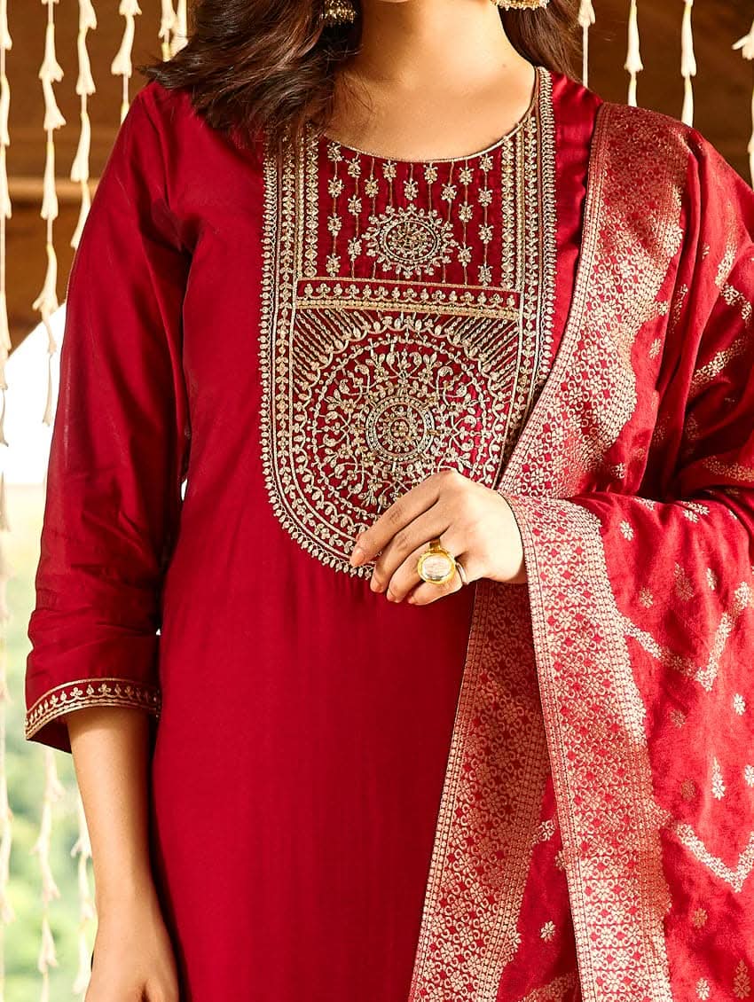 A woman wearing a red silk suit set with embroidered details and a dupatta.