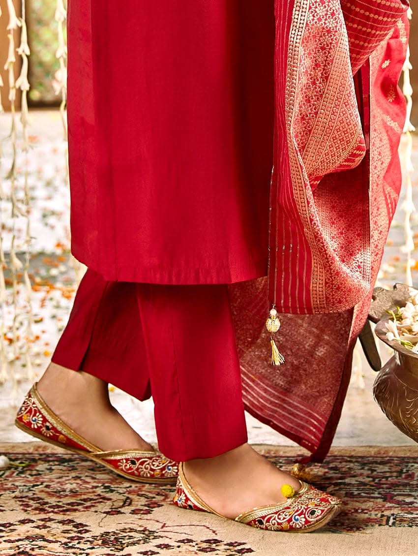 A woman wearing a red silk suit set with embroidered details and a dupatta.