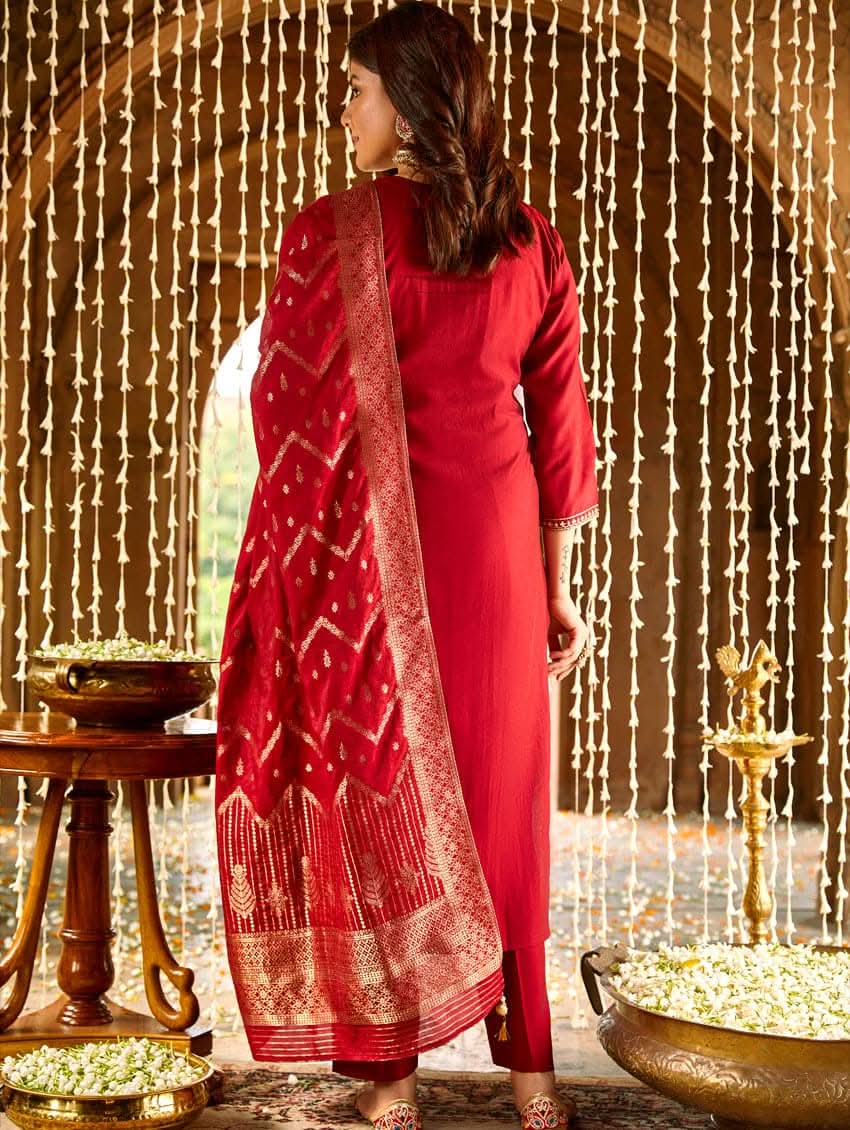 A woman wearing a red silk suit set with embroidered details and a dupatta.