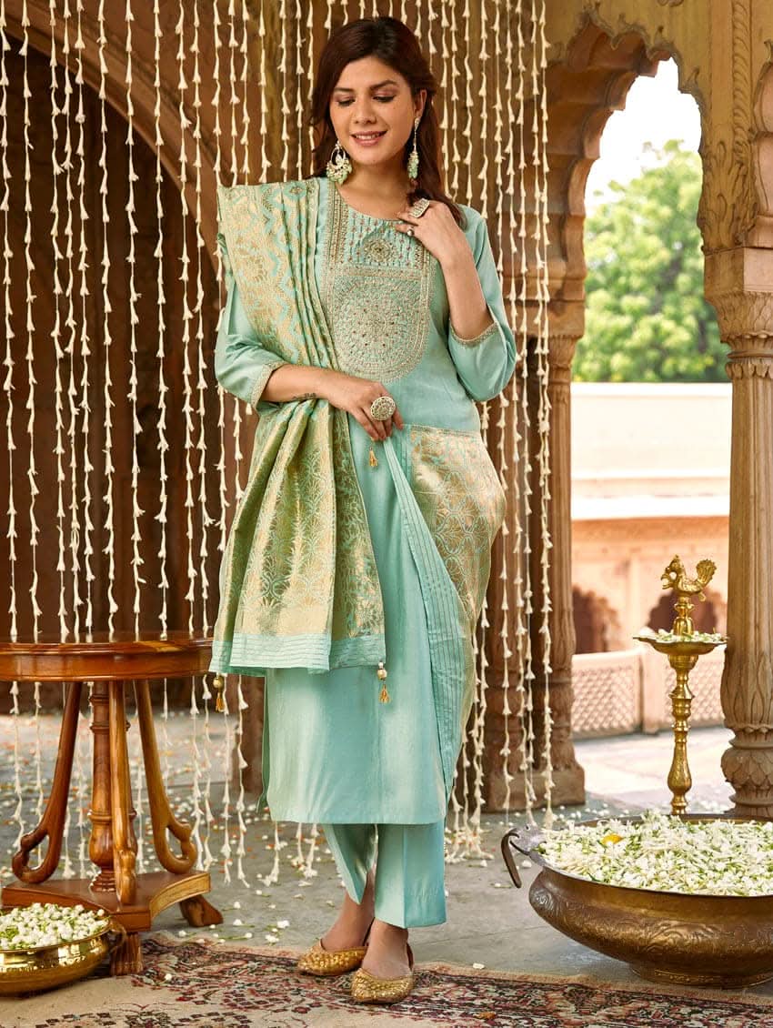 A woman wearing a sea green silk suit set with embroidered details and a dupatta.