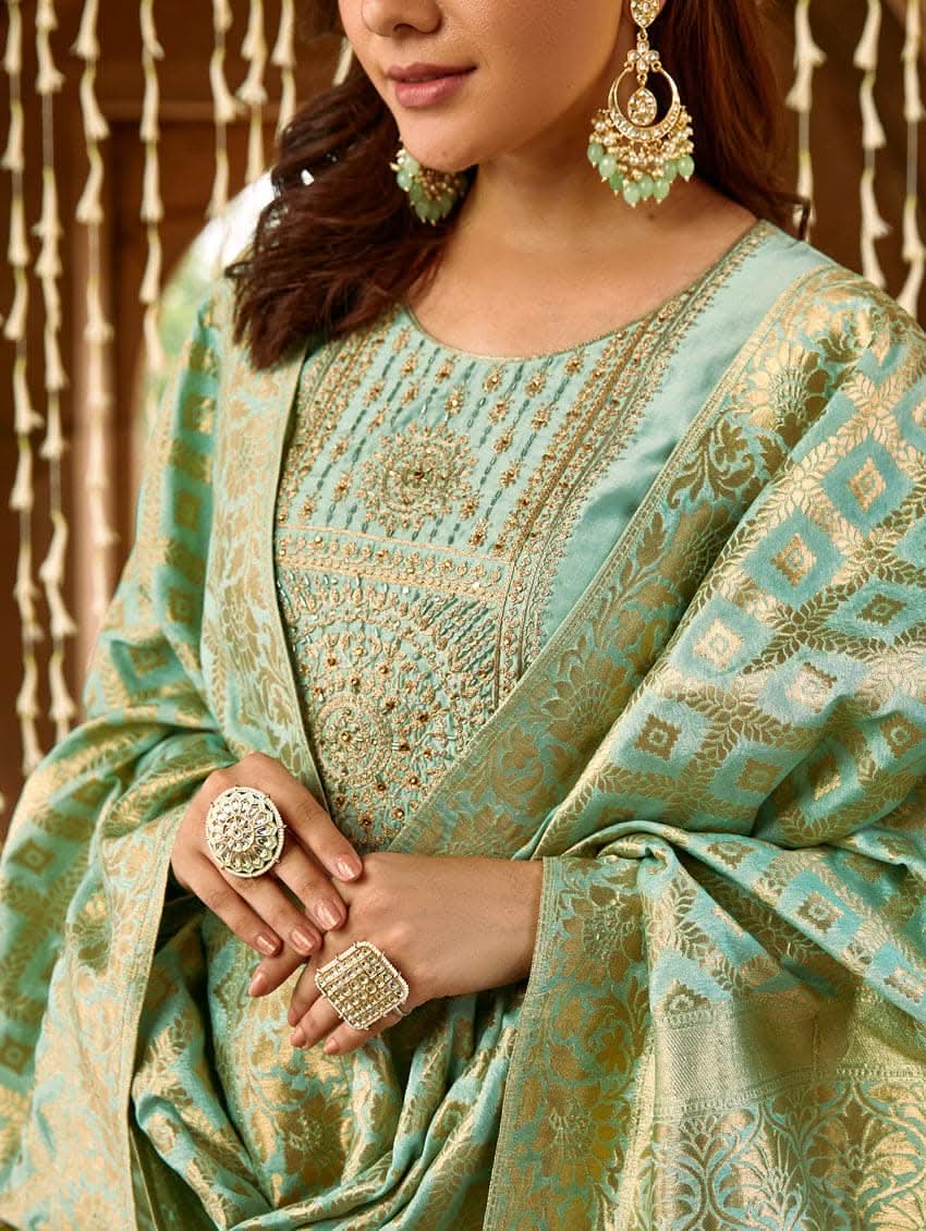A woman wearing a sea green silk suit set with embroidered details and a dupatta.