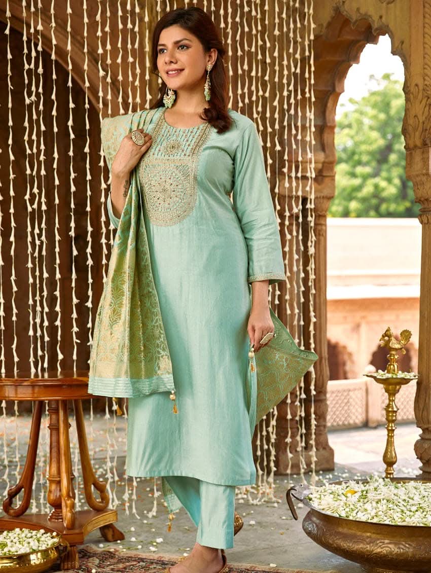 A woman wearing a sea green silk suit set with embroidered details and a dupatta.