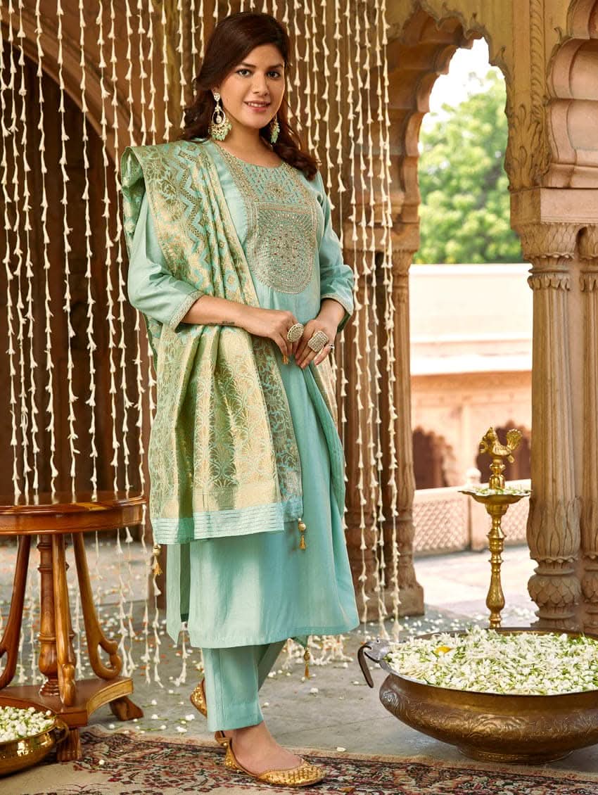 A woman wearing a sea green silk suit set with embroidered details and a dupatta.