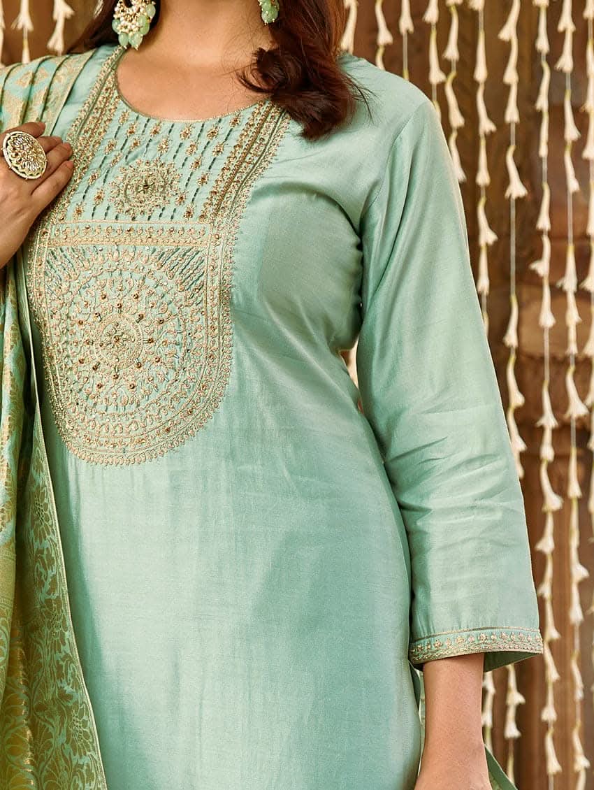 A woman wearing a sea green silk suit set with embroidered details and a dupatta.