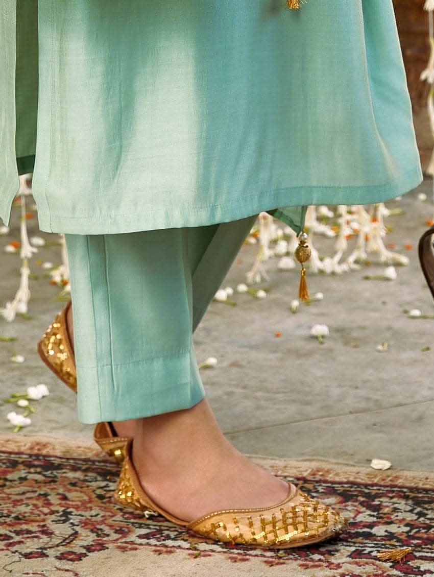 A woman wearing a sea green silk suit set with embroidered details and a dupatta.