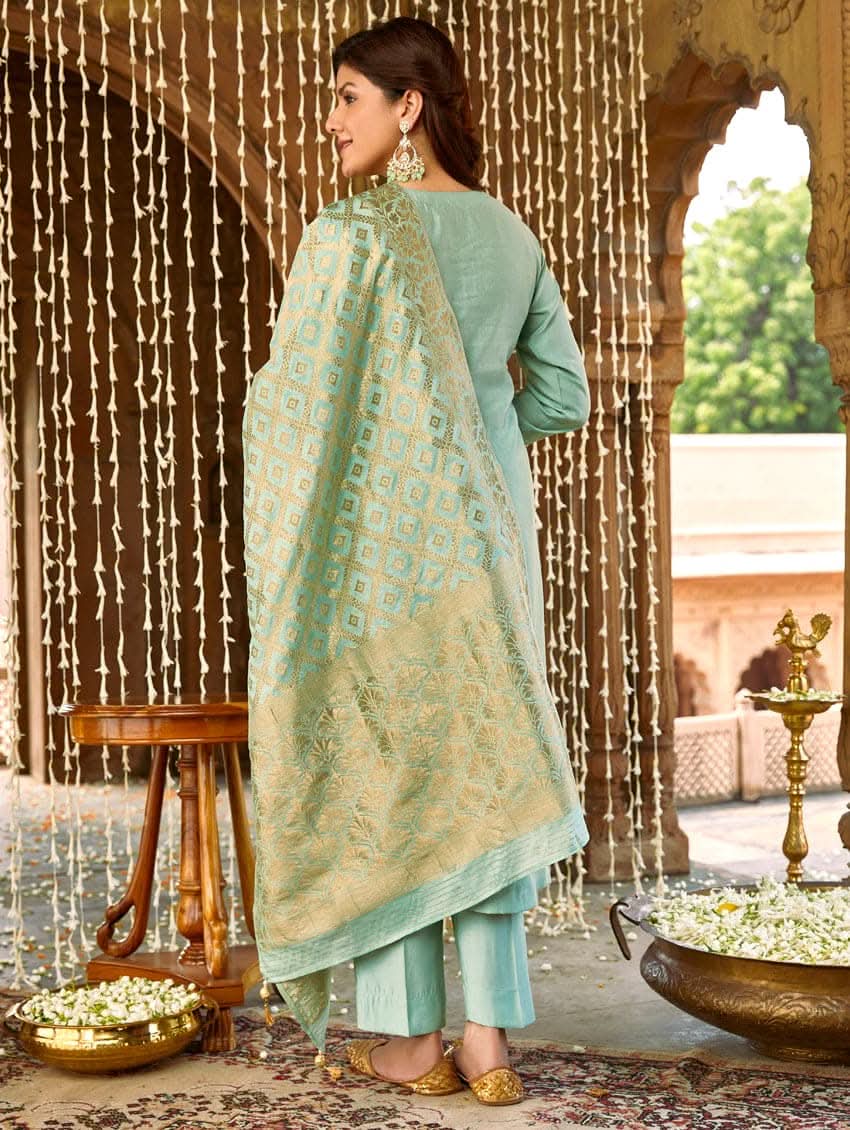 A woman wearing a sea green silk suit set with embroidered details and a dupatta.
