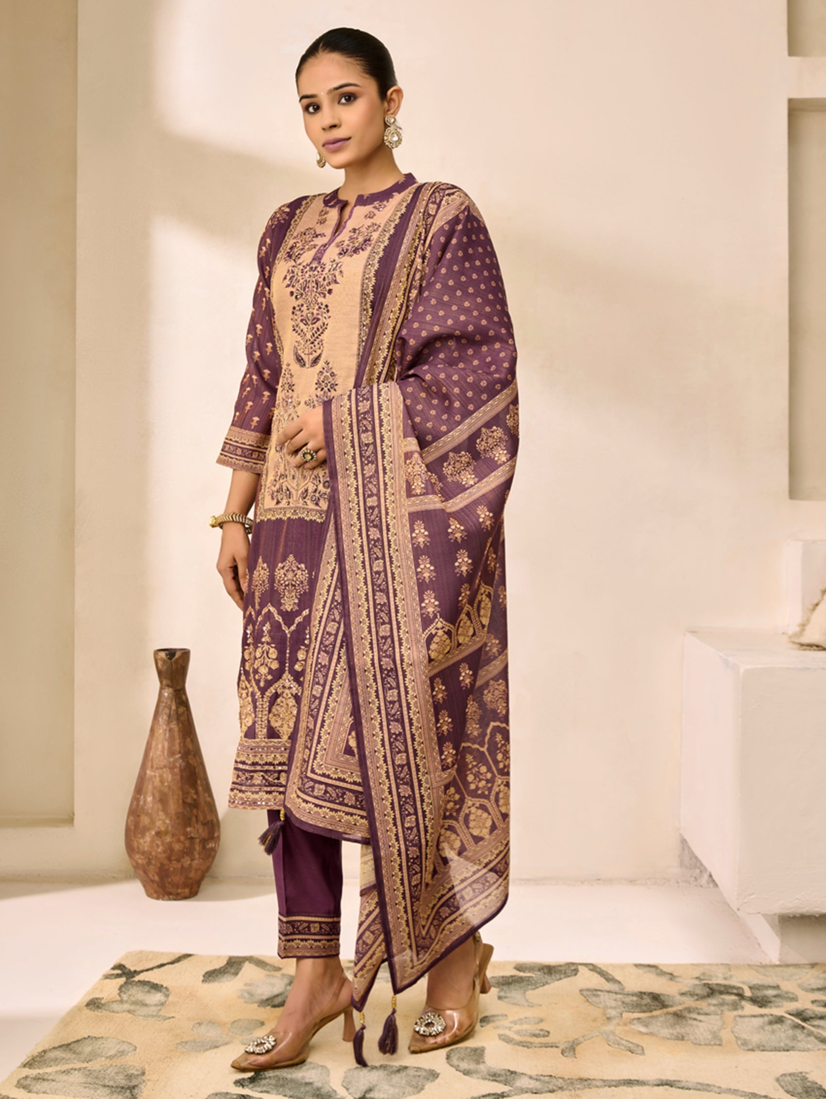 Woman wearing a traditional outfit with purple and beige patterns in a minimalistic setting.