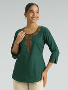 Woman wearing a green embroidered top against a plain background