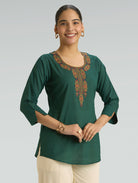 Woman wearing a green embroidered top against a gray background
