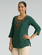 Woman wearing a green embroidered top against a gray background