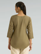 Woman wearing a green long-sleeve top against a gray background
