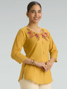 Woman wearing a yellow embroidered top against a gray background