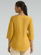 Woman wearing a mustard yellow top against a gray background