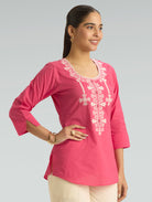 Woman wearing a pink embroidered top on a gray background
