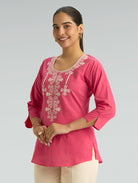 Woman wearing a pink embroidered top against a gray background