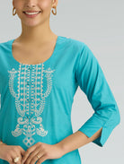 Turquoise top with white embroidery on a gray background