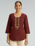 Woman wearing a maroon embroidered top against a plain background
