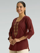 Woman wearing a burgundy top with floral embroidery on a plain background