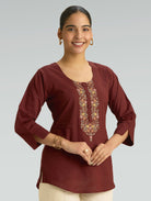 Woman wearing a maroon top with floral embroidery on a plain background