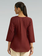 Woman wearing a maroon top with a plain background