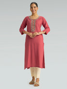 “A woman wearing a straight-fit pink kurta with a round collar and computerized thread embroidery on a gray background.”