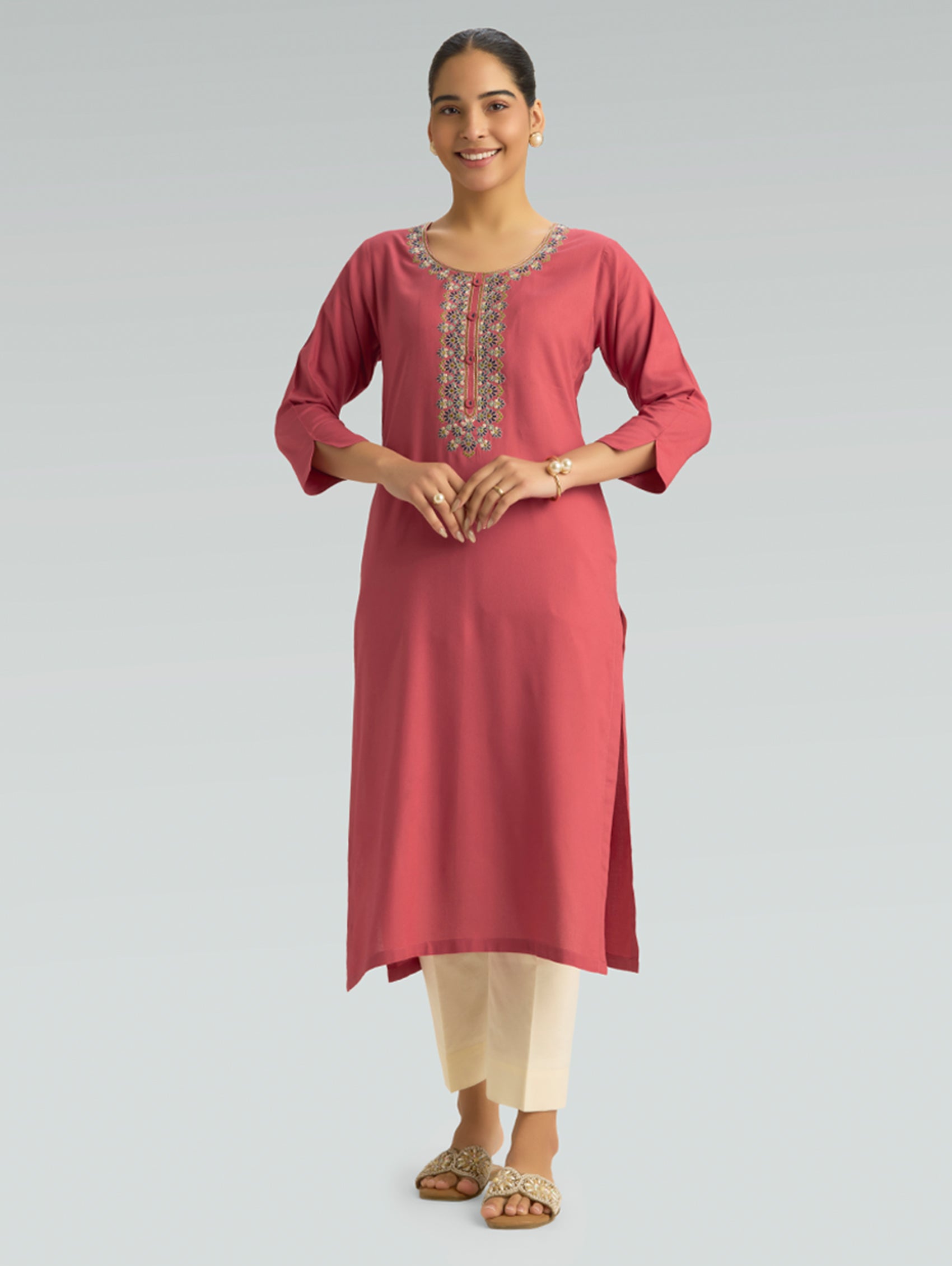 “A woman wearing a straight-fit pink kurta with a round collar and computerized thread embroidery on a gray background.”