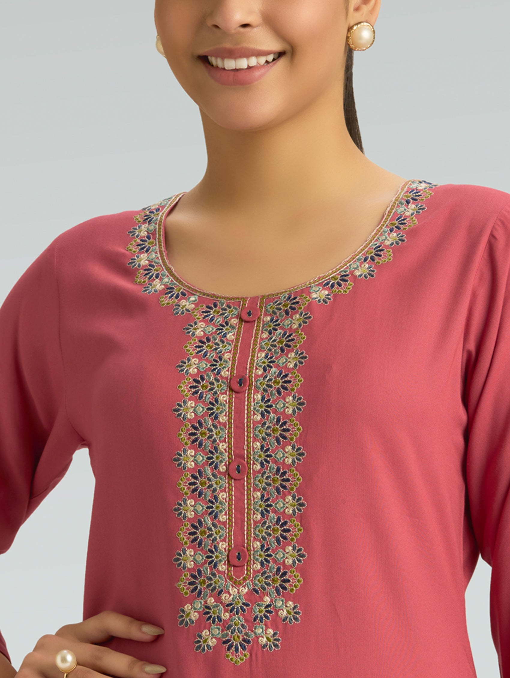 Pink embroidered top worn by a model on a gray background