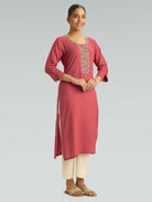 Woman wearing a pink kurta with white embroidery on a gray background