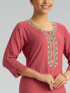 Woman wearing a pink kurta with intricate embroidery on a gray background