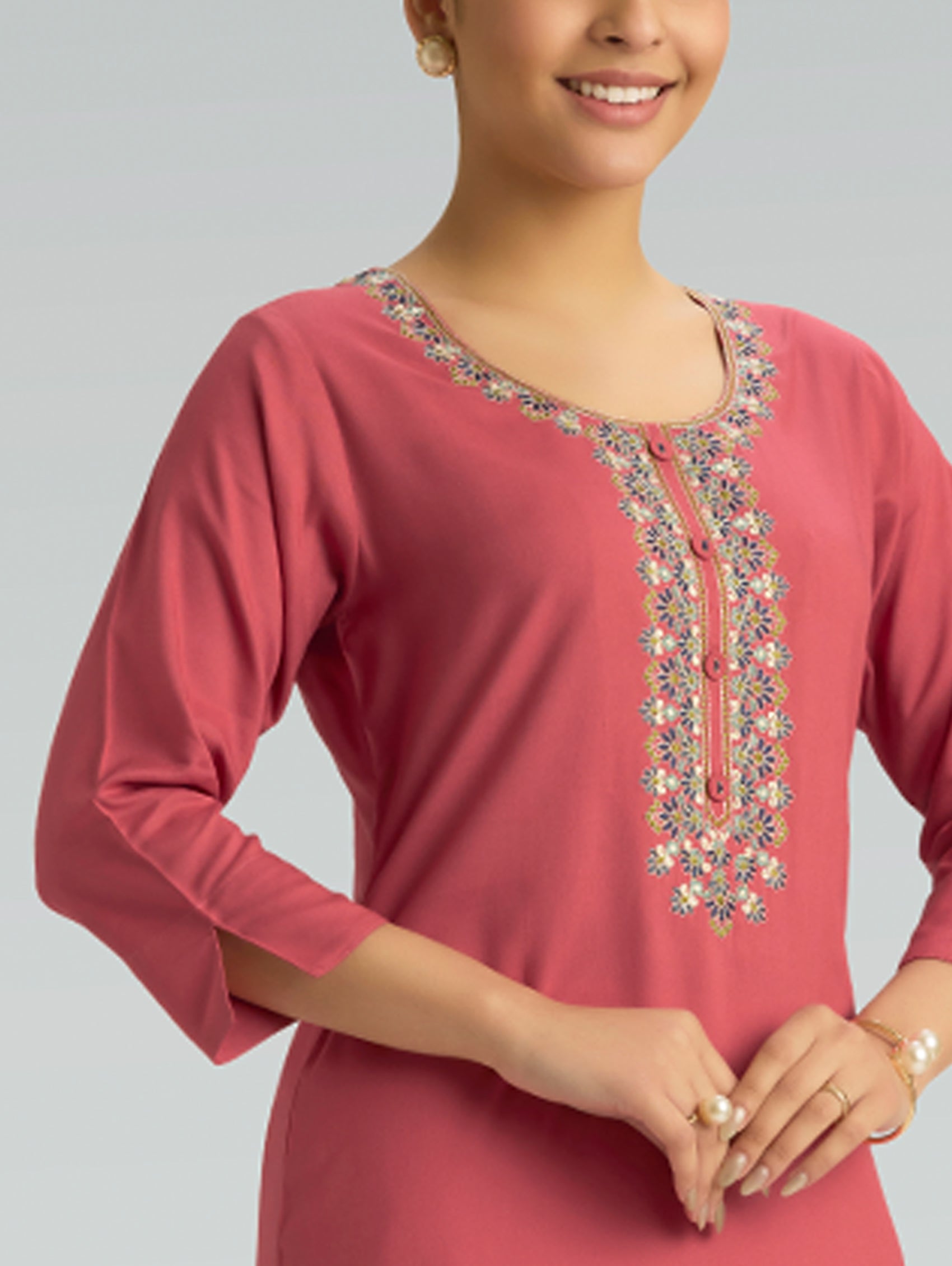 Woman wearing a pink kurta with intricate embroidery on a gray background