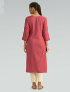 “A woman dressed in a pink kurta with beige pants, captured in a graceful back pose against a light gray background.”